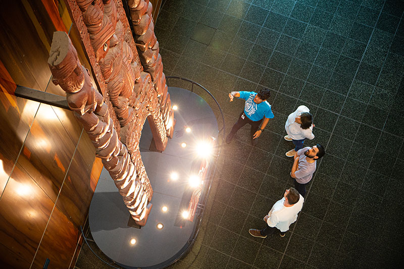 A Te Papa host points at a waharoa (a gateway) on display while visitors look on