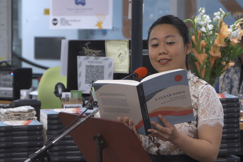 A woman stands in front of a microphone reading from a book in a book store