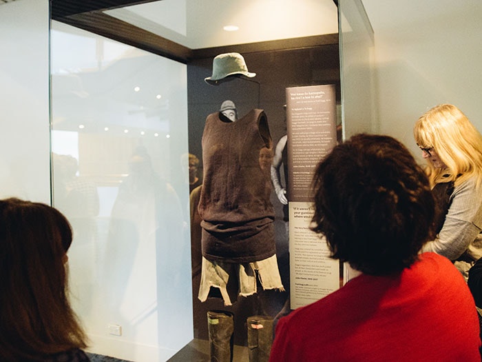 People look at the Fred Dagg costume - hat, singlet, shorts, and gumboots - in a display case