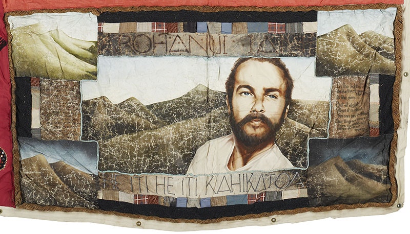 Panel of a quilt showing a portrait of a man and various scenes of mountains. It reads Arohanui Ian, He iti he iti kahikatoa