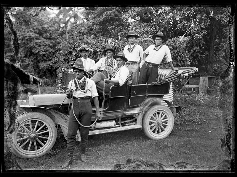 five men in cowboy outfits in an old car and one man in a cowboy outfit standing next to the car