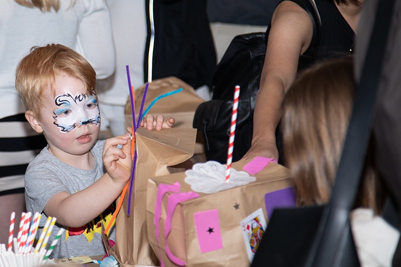 A child with facepaint on is making something with paper bags, straws, and coloured pipecleaners.
