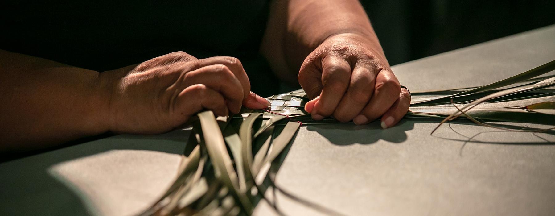A close-up of two hands weaving some green flax.