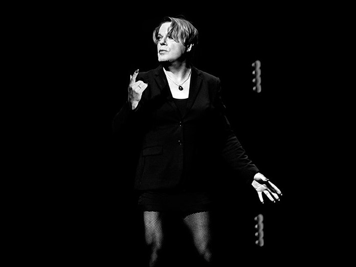 Eddie Izzard, Shakespeare's Hamlet, 2026. Photo by BOHM A person in fishnet stockings and a suit jacket is on a dark stage under a spotlight.