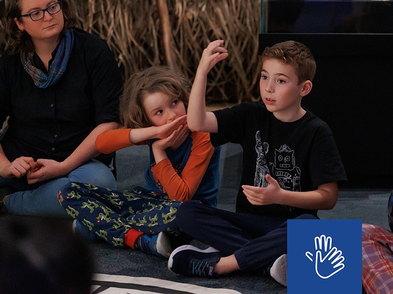 Matariki Whānau Day 2025 Te Papa, photo by Jo Moore. Te Papa (268353) A child is sitting on the floor and making actions with his hands. There is another child next to him and an adult.