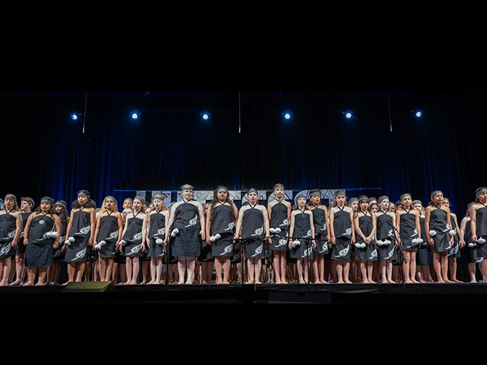 Hutt Fest. Photo by Lisa Preston Photography A line of intermediate school children on a stage. They are dressed in their Kapa Haka outfits.