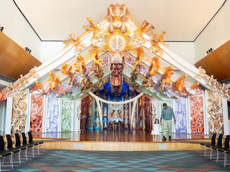 Rongomaraeroa, 2019. Te Papa A father and daughter hold hand on an ornately carved wharenui (large meeting house)