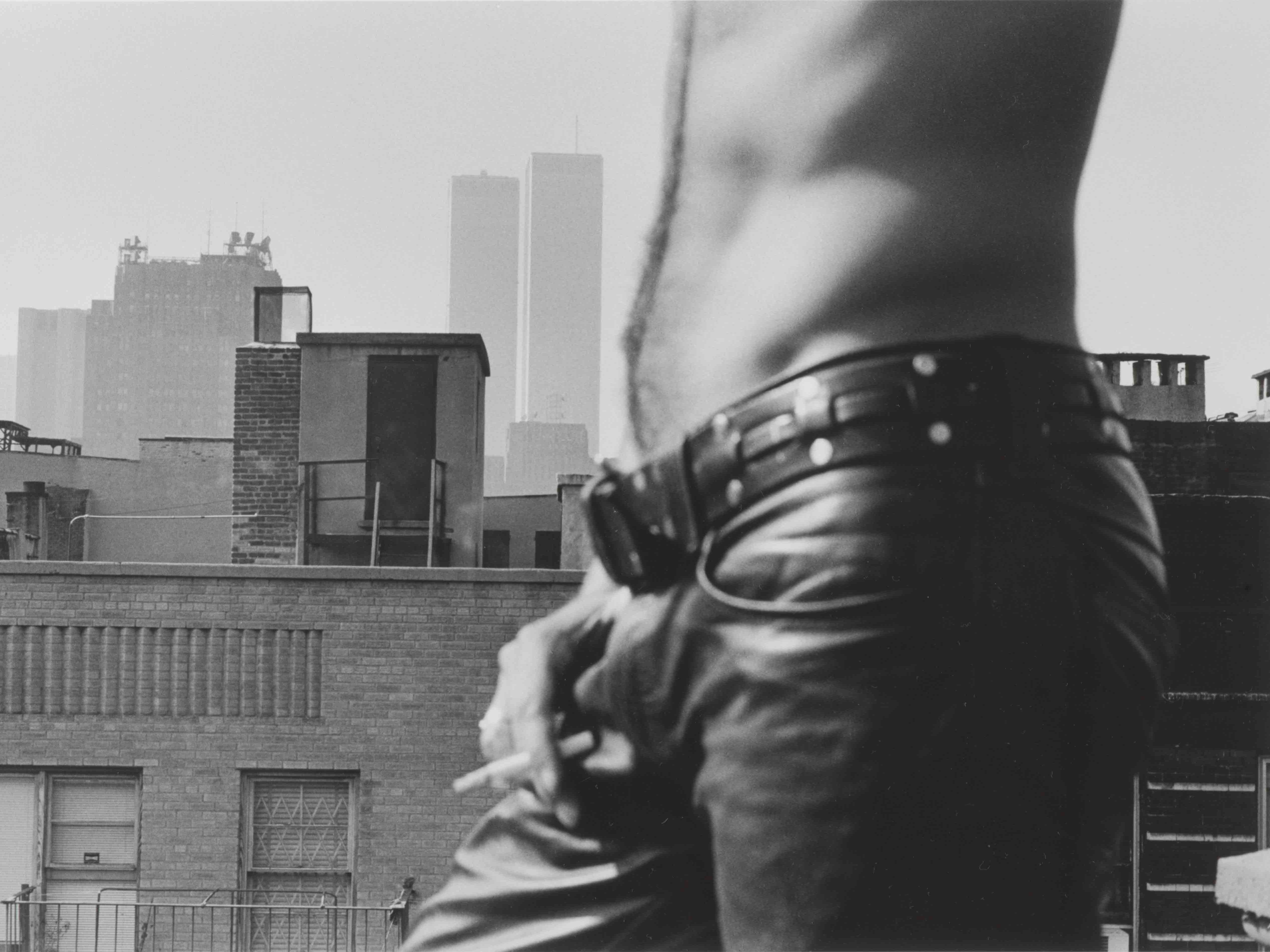 Alexis Hunter, Untitled. From the Object Series, 1974-75, black and white photograph, gelatin silver print. Purchased 2008 (O.031448) A black and white photograph of a man's torso. He is wearing jeans and smoking, standing on a roof with a city in the background.