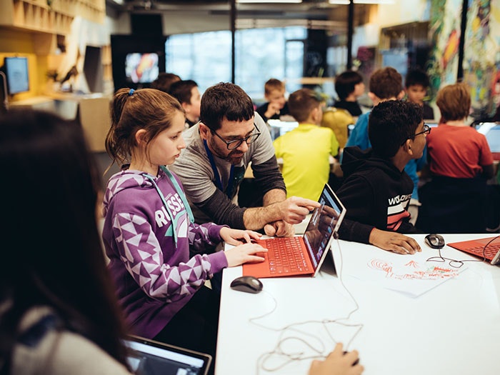 Hīnātore After School Club, 2017. Te Papa A man shows a young girl something on a computer in busy room