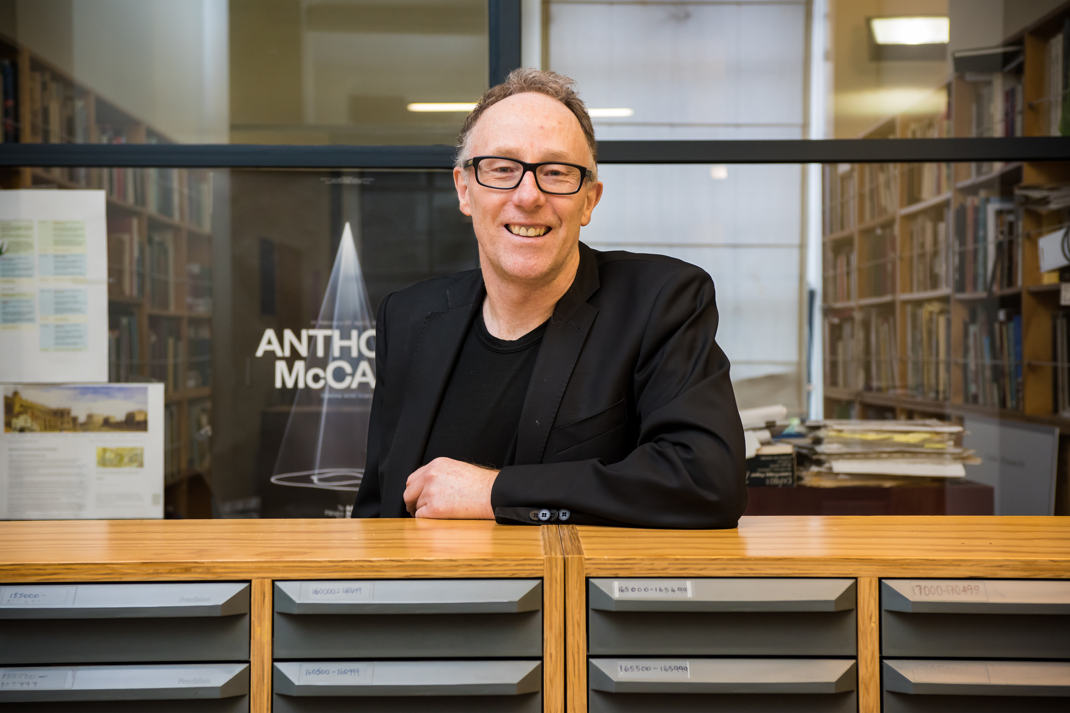 A man leaning on a filing cabinet and smiling at the camera