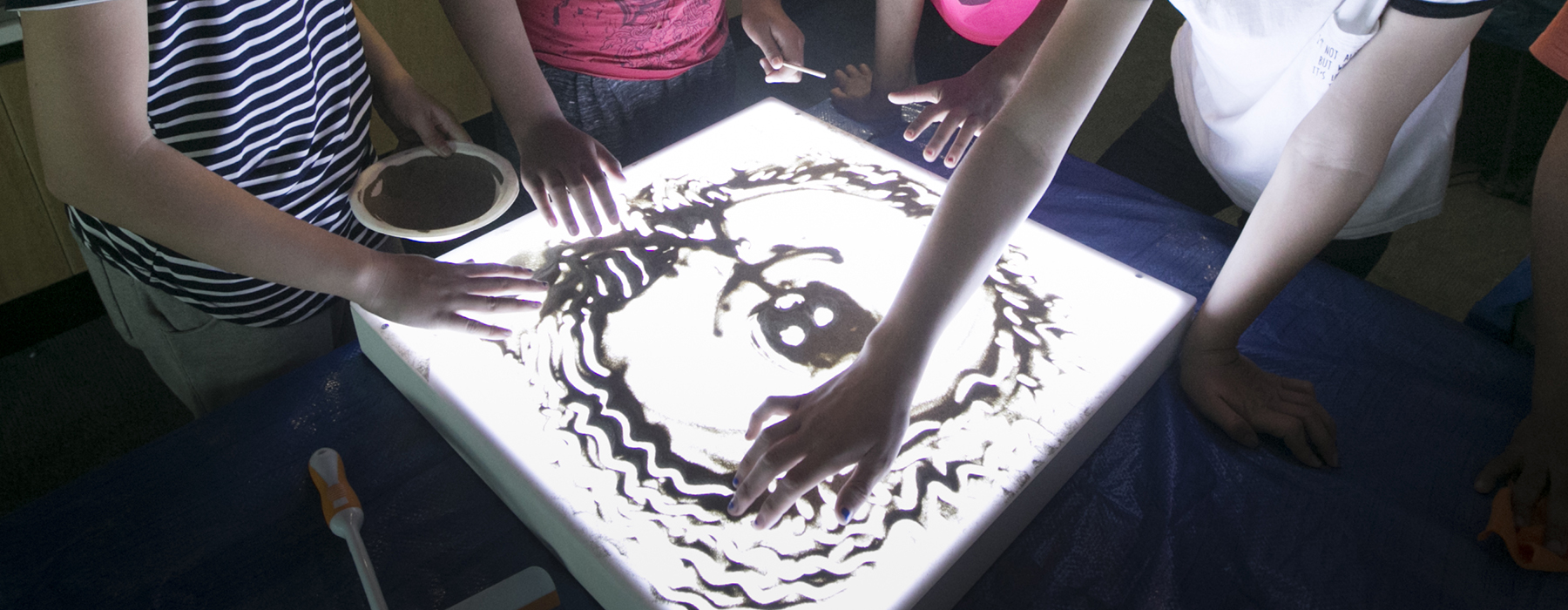 Children drawing on a sandbox (a light box with sand on top of it)