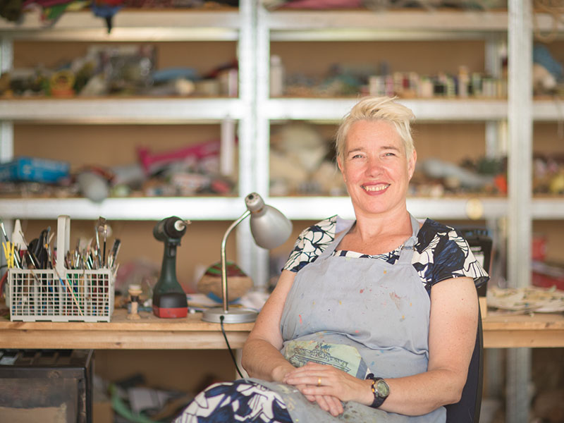 Lisa Walker sits in her studio, with shelving behind her full of materials