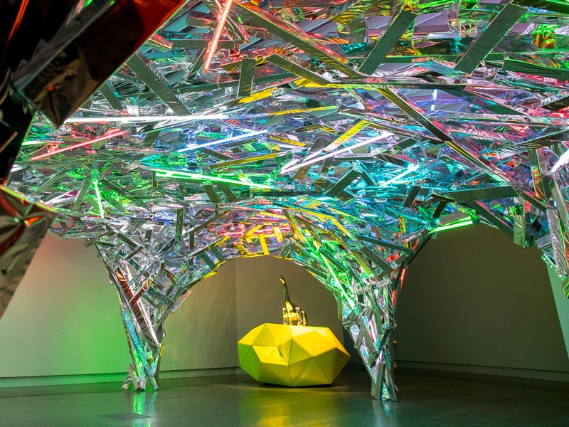 Anthropocene Shelter, 2018 by Gregor Kregar in Curious Creatures & Marvellous Monsters, 2018. Photograph by Maarten Holl. Te Papa (111224) A shiny colourful artwork featuring a metal dinosaur