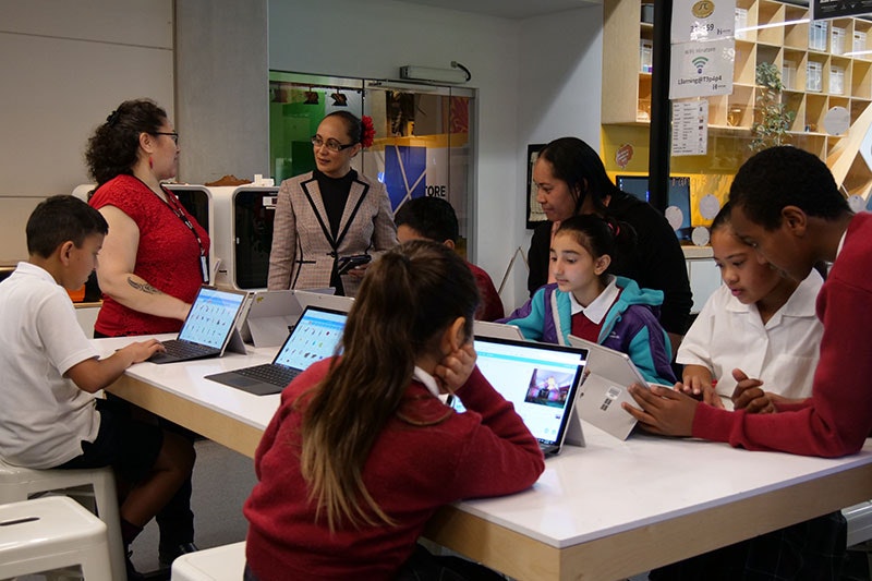 Students and teachers work at a desk full of computers
