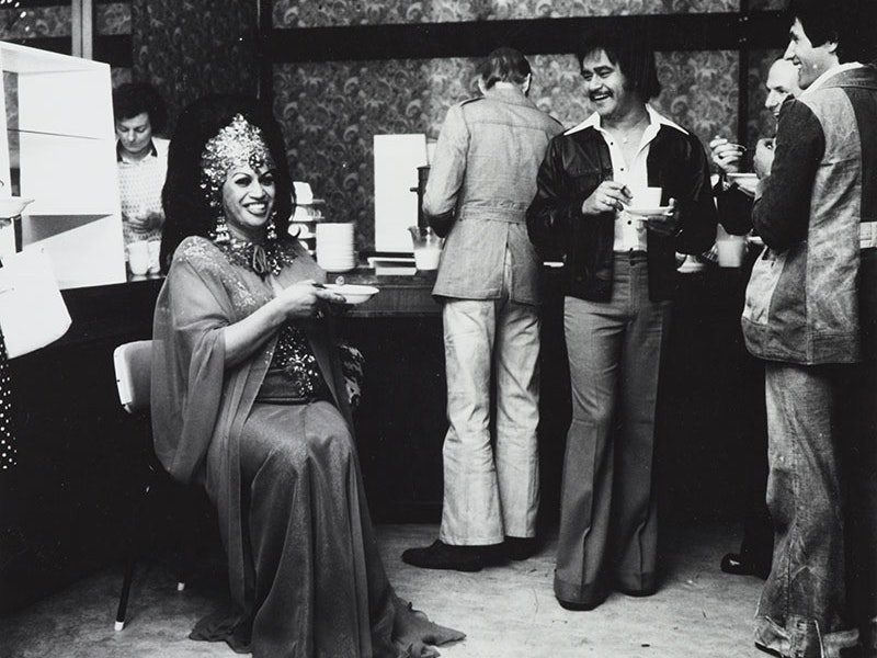 Maoritanga - Scenes from Maori Life, Carmen, by Ans Westra, 1970s, Wellington. Purchased 1993 with New Zealand Lottery Grants Board funds. Te Papa (O.016233) Carmen sits with a bowl while several men stand around with coffee cups and bowls in front of what appears to be self-serve breakfast