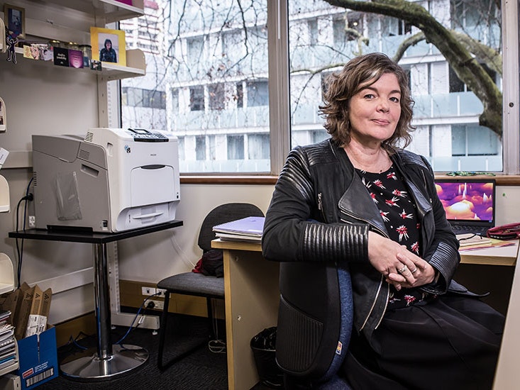 Professor Juliet Gerrard, 2018. Photo by Simon Young / simonyoungphotographer.com Juliet sits at her desk, with her arm over the back of the chair, in her office. Behind her is a large printer and shelves with books and framed photos