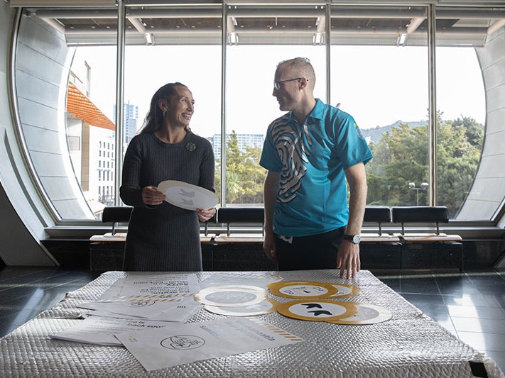 Chief Executive Courtney Johnston and Head of Visitor Services Shaun Pallett review information posters about Te Papa’s new hygiene measures. Photo by Jack Fisher. Te Papa Two people stand in front of a table with an array of safety notices on it