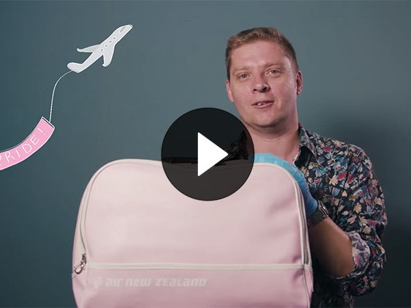 Still from What makes a queer object?, 2020. Te Papa Chris Brickell holds a pink Air New Zealand travel bag. An illustration of an aeroplane flies behind him with a pink flag saying ‘Pride’ behind it