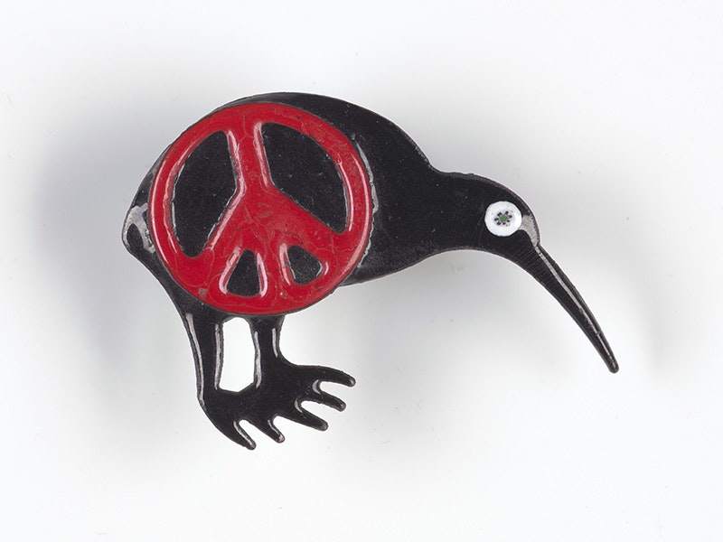 A black enamel kiwi with a red Peace sign on it, sitting on a white background