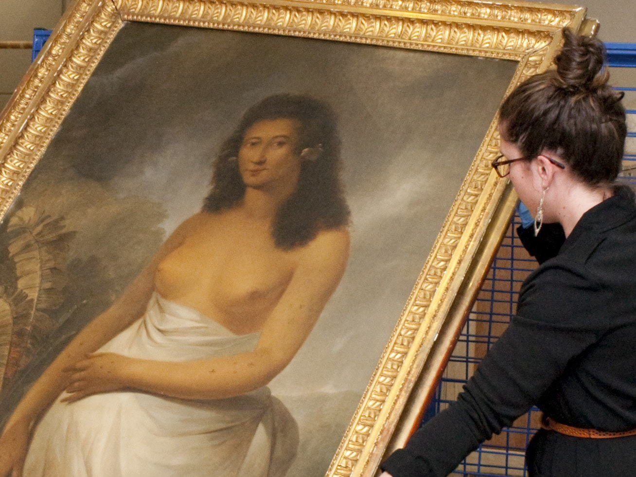 Te Papa conservators with John Webber's Poedua. Photograph by Kate Whitley. Te Papa A woman holding a painting wearing blue gloves