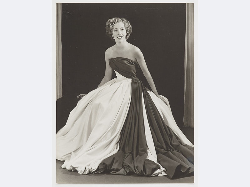 Mary-Annette Hay in Maggy Roulf cherry red and white gown, Anderson and Atkinson; photographer; 1951-1952; Wellington. Te Papa (CA000921/001/0001/0008) A black and white photo of a woman in a long dress