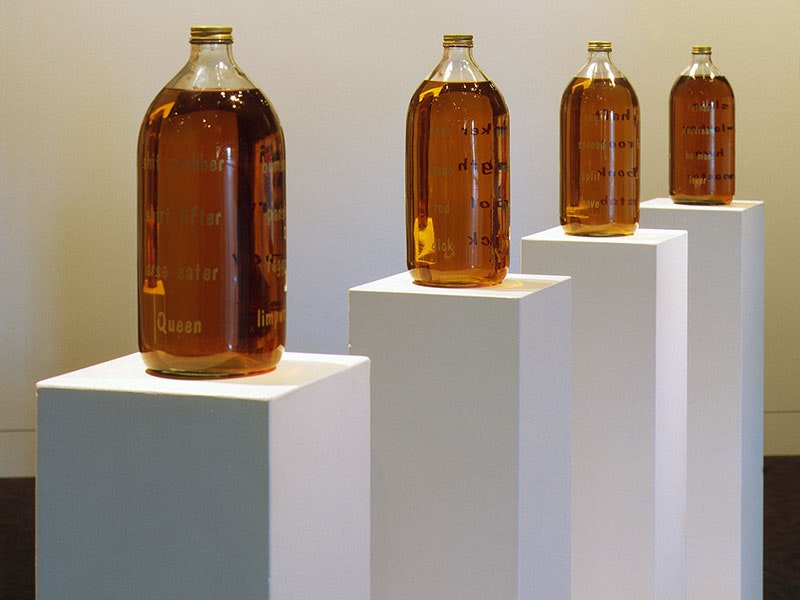Grant Lingard, Strange bedfellows, 1993, glass, metal, vinyl lettering, beer, wooden plinths. Te Papa (1996-0030-1/A-H TO H) Four large bottles containing beer stand on four plinths