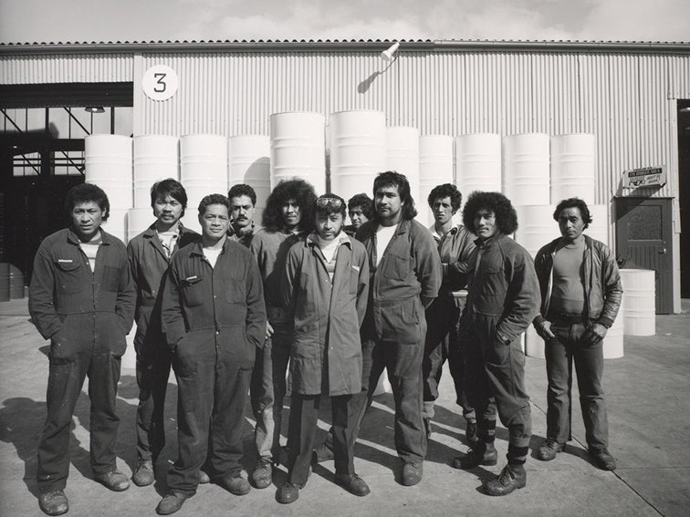 10.5.1982. Rheem Industries, Rosebank Road, Avondale, west Auckland. 44 gallon drum assembly line workers by Mark Adams, 1982. Purchased 1993 with New Zealand Lottery Grants Board funds. Te Papa (O.004103) Black and white photo of 11 men in overalls standing in front of a factory