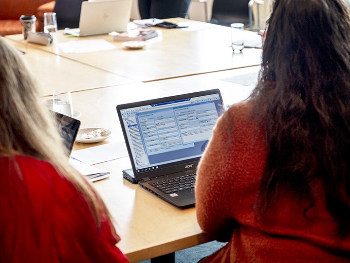 National Services Te Paerangi repatriation workshop, 31 Mar 2021. Photo by Daniel Crichton-Rouse. Te Papa (168646) People gathered around a table with computers, there is a woman in the foreground looking at a screen.