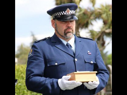 A man in a police uniform holding a small wooden box in gloved hands