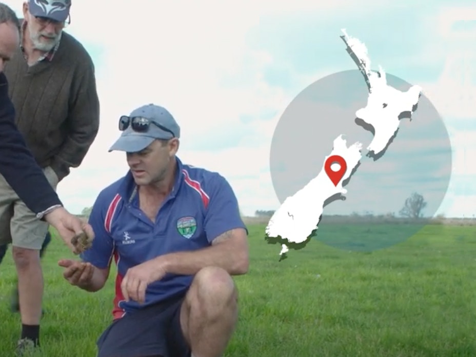 Video still from Regenerative farming, Canterbury. Te Papa Men looking at something on the grassy ground. There's a map of New Zealand overlaid on the image on the top right-hand side.