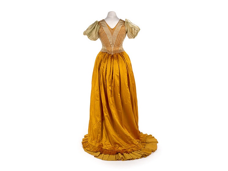 Evening Dress, about 1890, London, by Mrs Oliver, Modes & Robes. Gift of Joan Moore, 1984. CC BY-NC-ND 4.0. Te Papa (PC002880) A full-length yellow silk dress from the 1890s on a white background