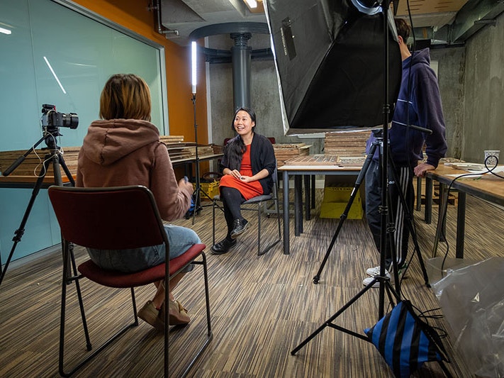 Shijia Chen interviews Ya-Wen Ho at Victoria University of Wellington, 2021. Photo by Grace Gassin. Te Papa A woman sits on a chair in the middle of a room, being interviewed by another woman sitting opposite her. A large light shines on the subject
