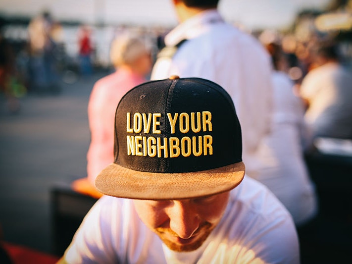 Photo by Nina Sterhl via Unsplash Close up of a man wearing a black cap. On the caps are the words ‘Love your neighbour’