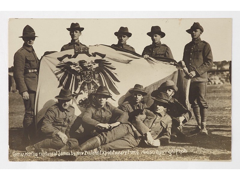Postcard, 'German War Flag captured at Samoa by New Zealand Expeditionary Force', 1914-1916, New Zealand, by William Wilson. Purchased 2011. Te Papa (GH023107) 10 people in uniform standing and sitting around a flag