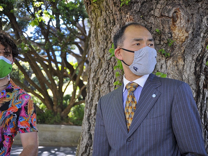 Henry Liu, right, with Director of Photography Tim Hamilton on location outside Parliament grounds, Wellington, 10 Nov 2021. Photo by and courtesy of Shijia Chen Henry stands in front of a large tree looking into the distance. Tim stands beside him looking in the same direction