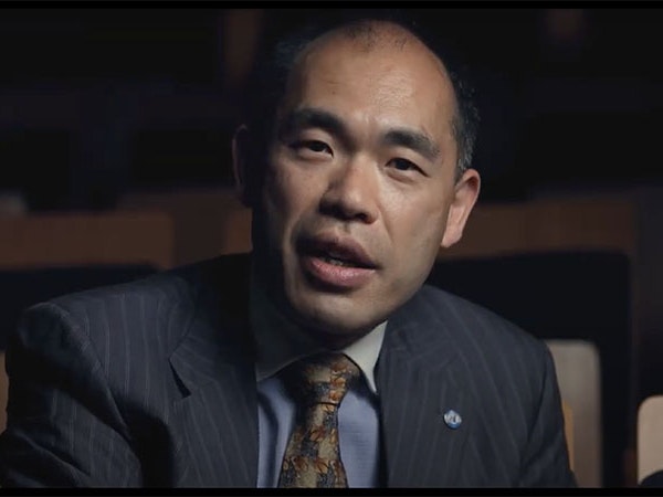 Video still from Chinese Languages in Aotearoa: Hakka, with interpreter Henry Liu, 2022. Te Papa Henry Liu talks directly to camera in a darkened space