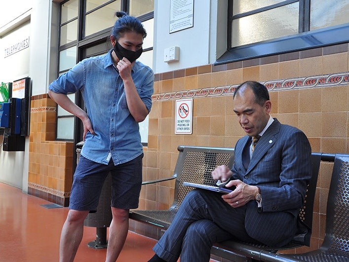 Yong-Le Chong (left) with Henry Liu during the film shoot for the Hakka video, 2021. Photo by Shijia Chen, courtesy of Shijia Chen Two men talking. One is seated looking at something on an iPad. The other is standing, also looking at what is on the iPad.