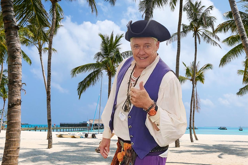 A man in a pirate costume is photoshopped onto a beach scene.
