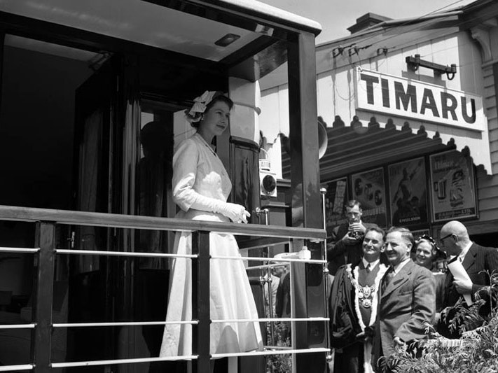 Queen Elizabeth II departing Timaru, 25 January 1954, by J G Duncan and R A O Morgan. Archives New Zealand Queen Elizabeth II stands on the back of the royal train at Timaru Station. A group of people stands beside the train