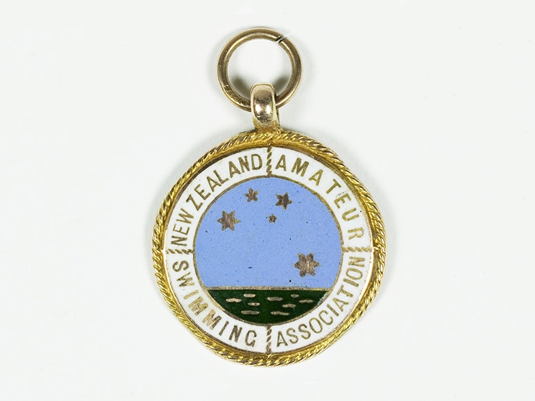 Sports medal, New Zealand Amateur Swimming Association, about 1928, Birmingham, by Thomas Fattorini Ltd. Gift of Margaret L Bailey, in memory of Jean A. Dickson, 2006. CC BY-NC-ND 4.0. Te Papa (GH021311) A round badge with gold edging and an image of the sea with the Southern Cross in stars above it. It has the words New Zealand Amateur Swimming Association on it