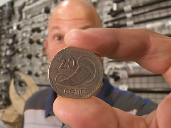 Still from Tales of A Whale Tooth Tale – Tales from Te Papa episode 116 A 20 cent coin held close to the camera with someone behind it