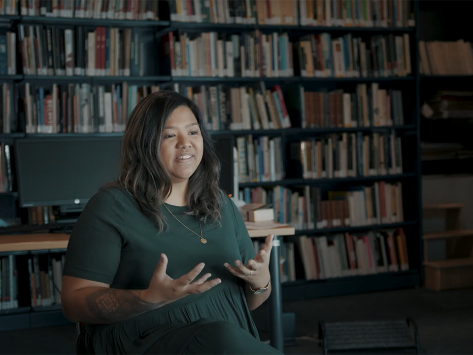 Video still of Maria Milmine talking about Asian mental health A woman in a green dress is talking to someone off camera and gesticulating with her hands.