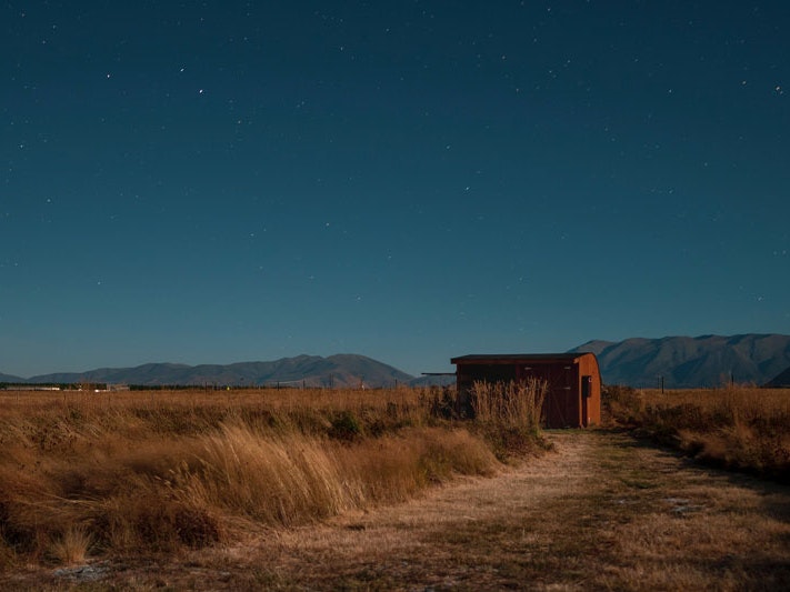 Twizel, 2019. Photo by Lawrence Makoona/Unsplash Photo of a country hut in the foreground and a star-filled night sky behind it