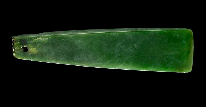 A pounamu greenstone chisel blade on a black background.