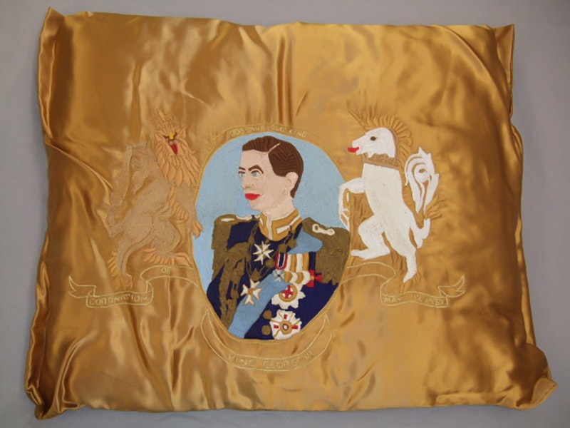 Embroidered cushion, King George VI, 1937, Dunedin, by Miss Nancy Robertson. Gift of The Merrick Girls, 2012. CC BY-NC-ND 4.0. Te Papa (GH017530) A gold satin cushion with an image of a king and a unicorn embroidered on it.