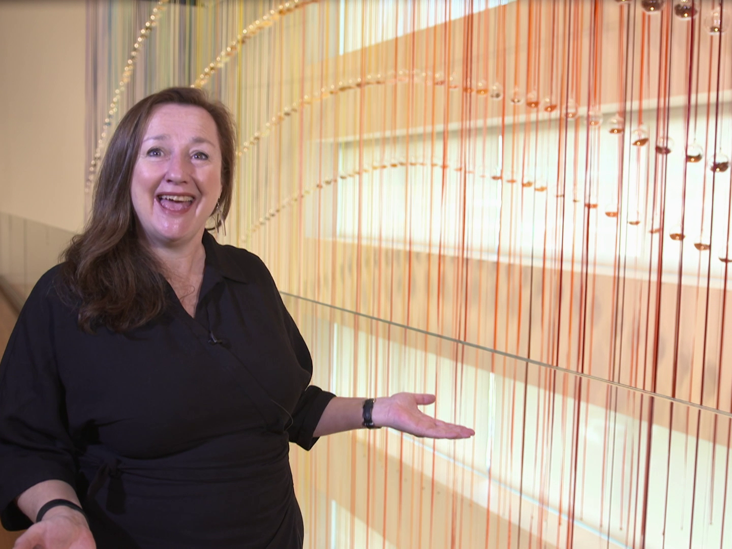 A still from Raranga Matahiko 8a and 8b. Te Papa A woman standing in front of a colourful art installation