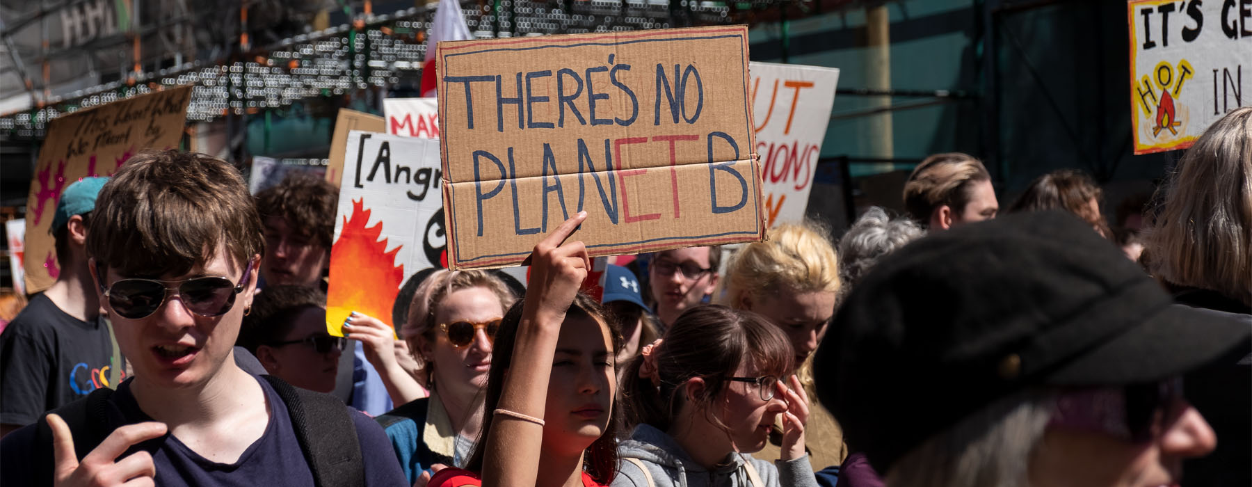 People marching down a street. A young woman holds up a sign that says “There’s no Planet B”