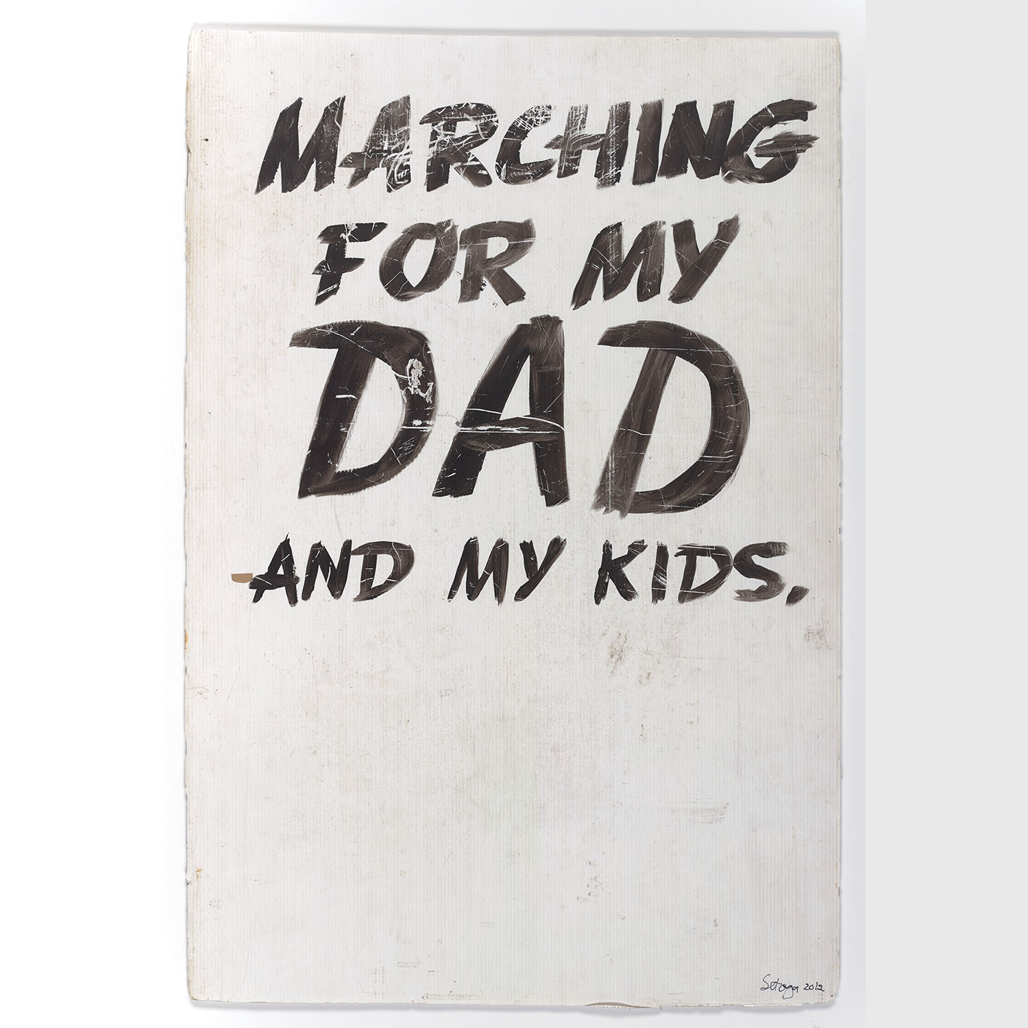 White rectangle of plastic with, painted in black, the words “Marching for my Dad and my kids”