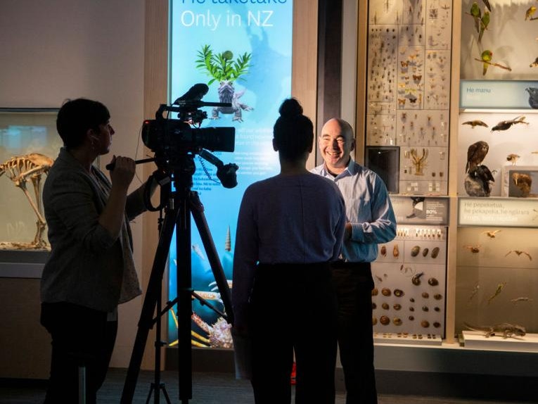 Curator Leon Perrie being interviewed, 2019. Photo by Michael O'Neill. Te Papa (136354) A man being interviewed in front of a large camera