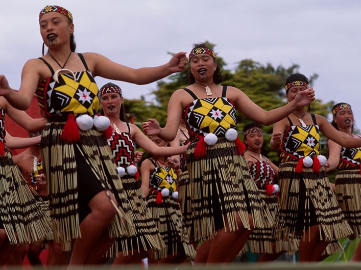 Poi group performing, by Glenn Jowitt; photographer; about 1990; New Zealand Women in traditional costume wearing white balls (poi) at their waists are singing and dancing in unison.